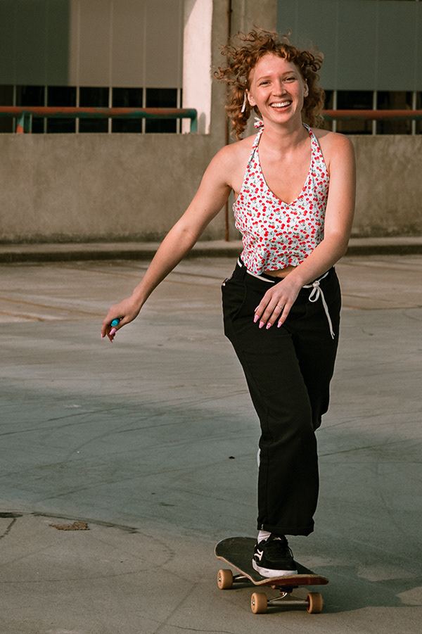 Young woman smiling as she rides a skateboard across the top of a parking deck