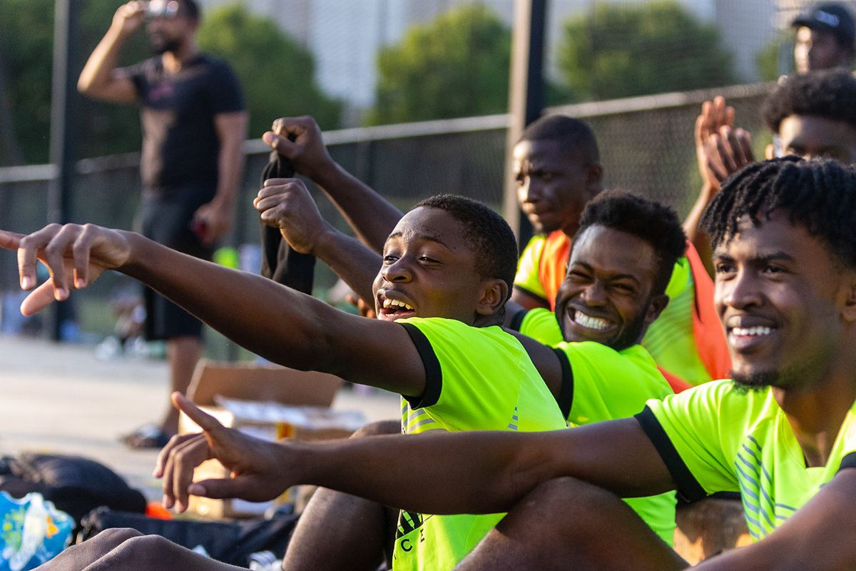 Greensboro International Football Club players in yellow bibs pointing and cheering from the sideline