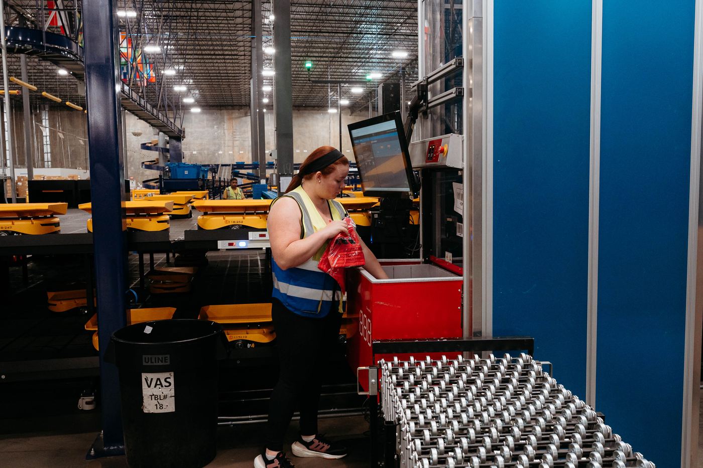 Worker at a pick station pulling an item from a red robot port