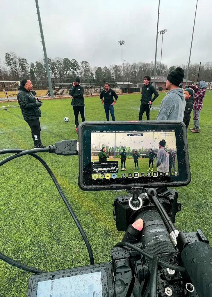 Camera monitor showing the shot of soccer players on a wet field, the players beyond it