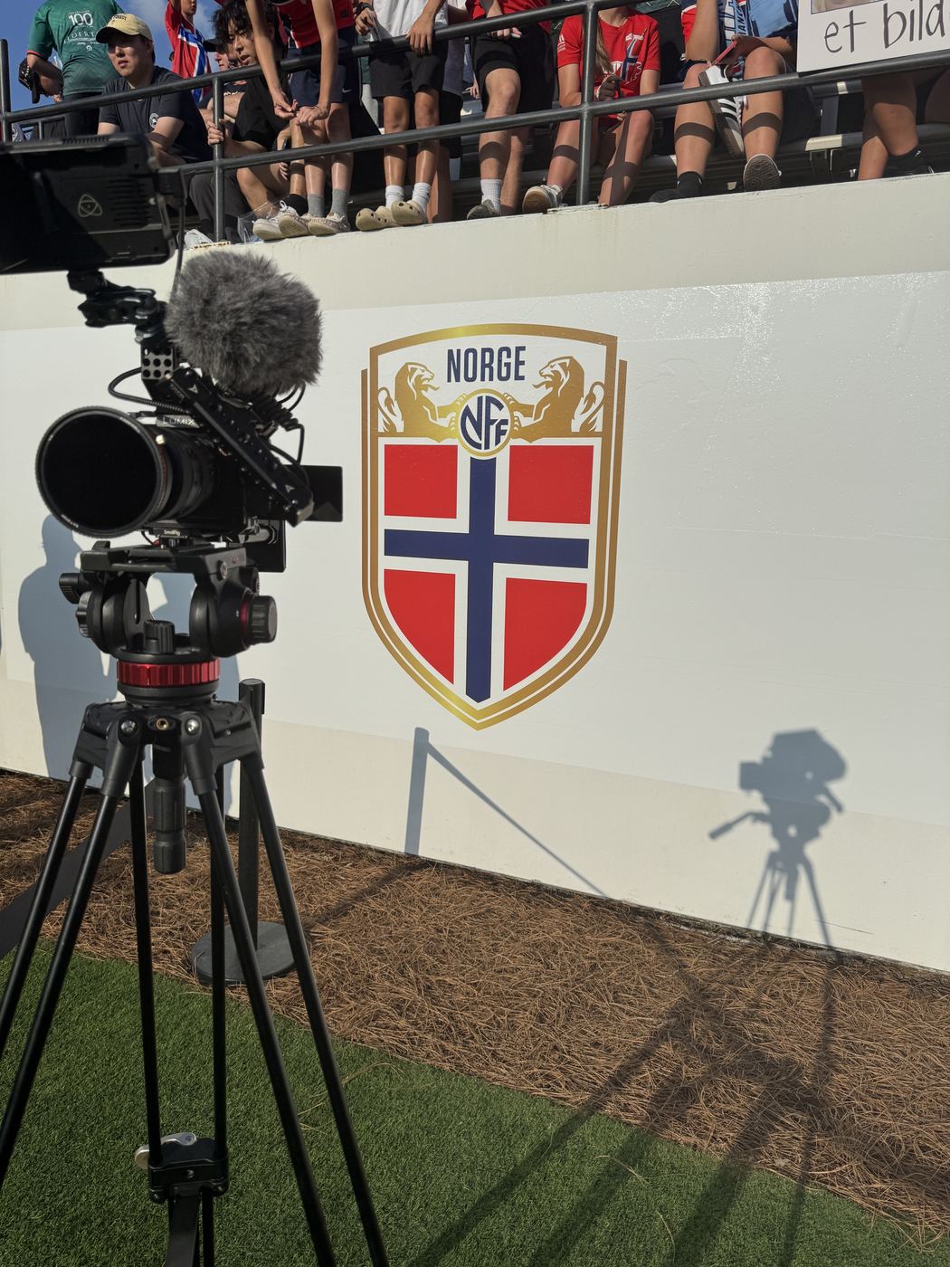Camera on a tripod against a stadium wall with a national team crest