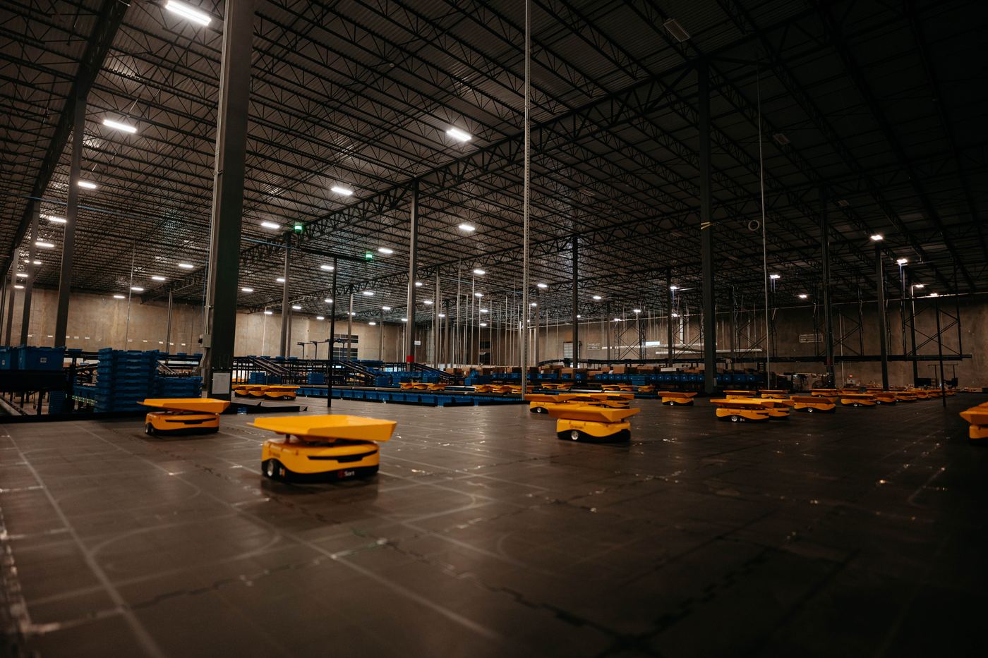 Yellow sort robots spread across a dark warehouse floor
