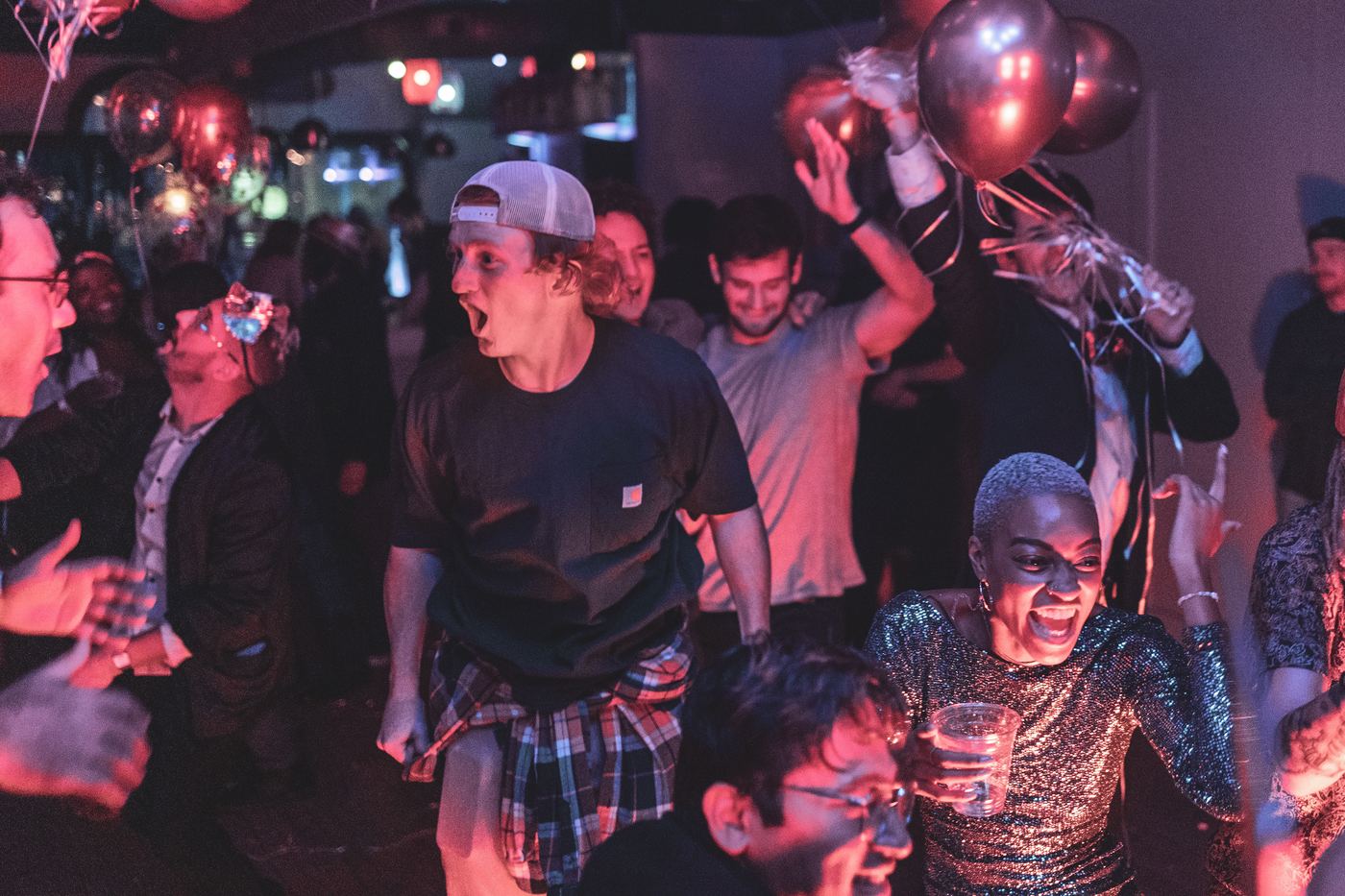 Crowd cheering and dancing under balloons at a New Year's Eve party
