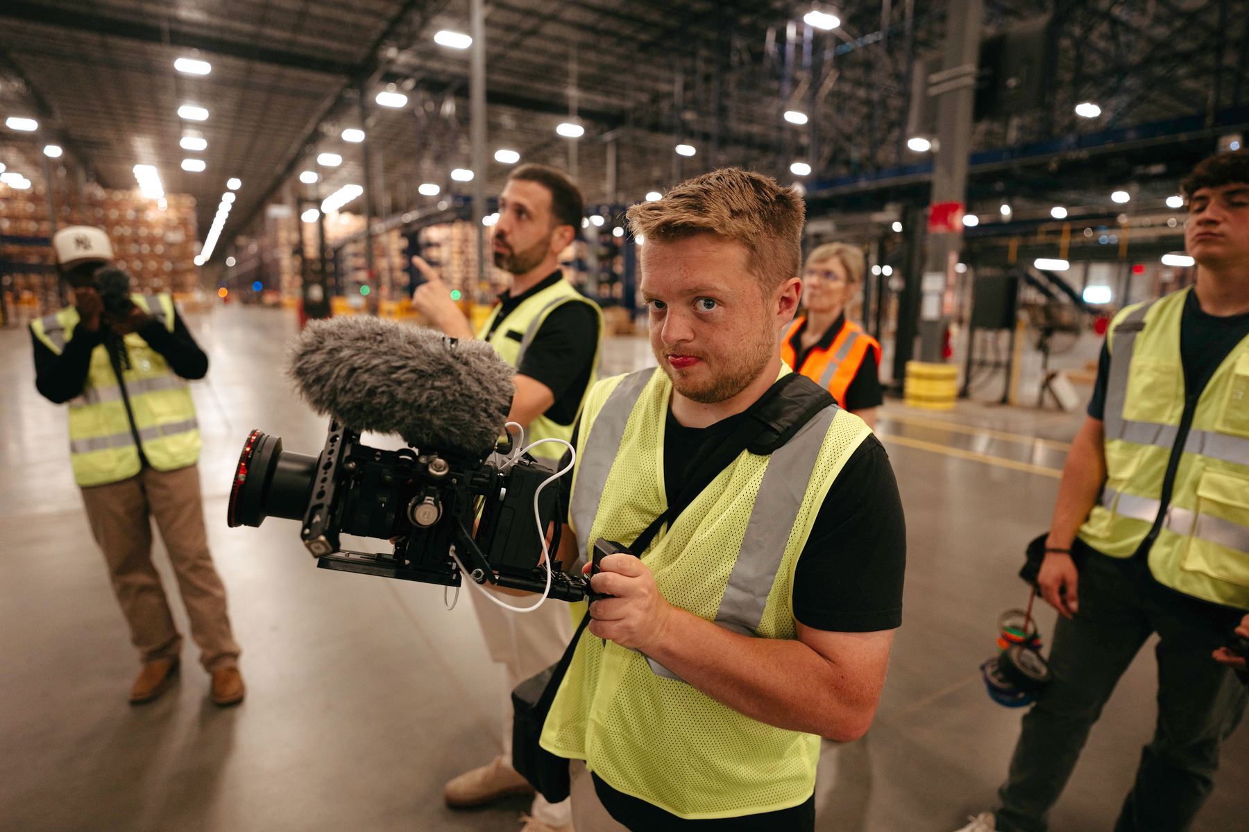 Dylan Smith holding a camera on a warehouse floor, the crew in safety vests around him