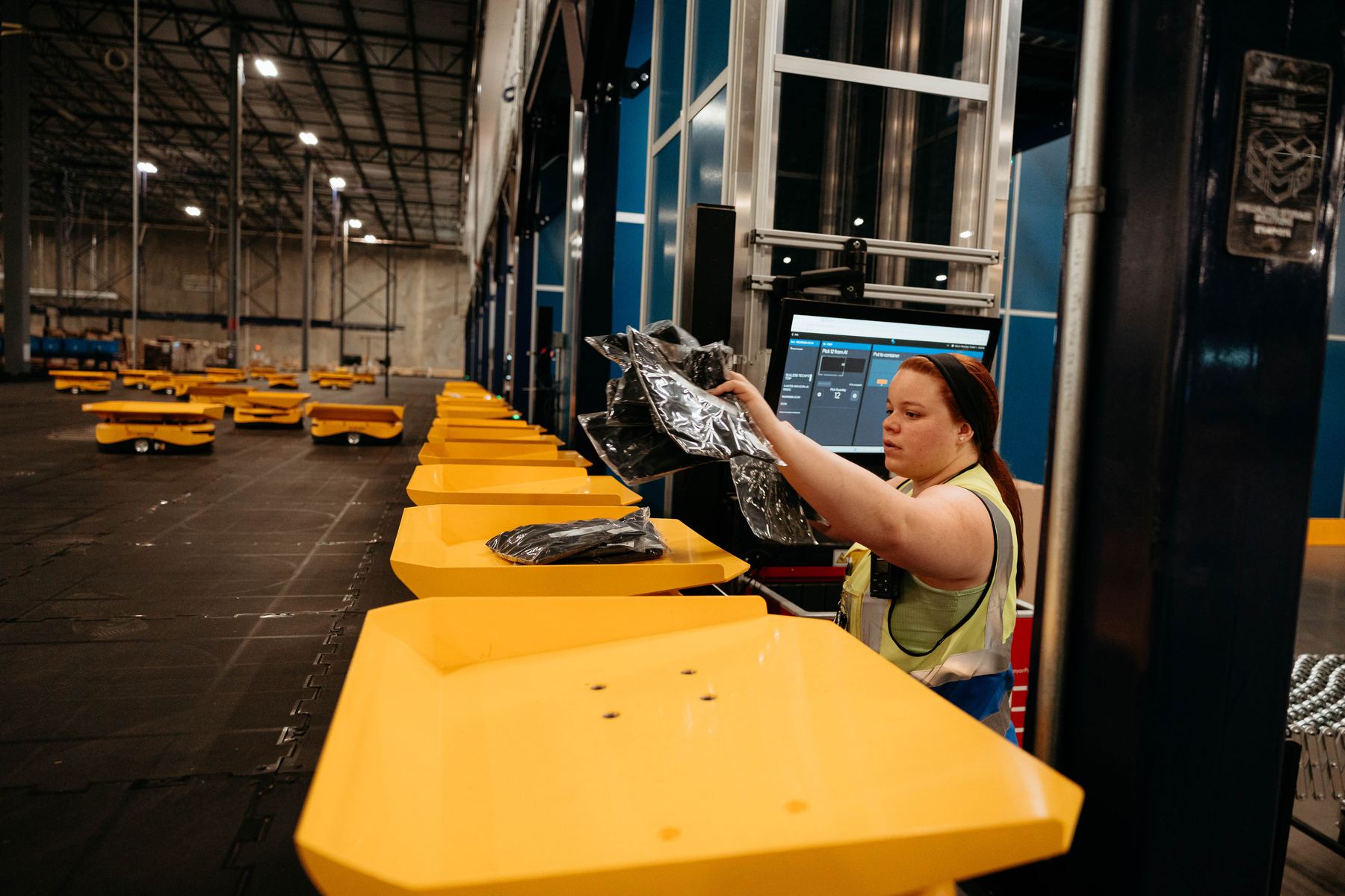 A warehouse worker loading a package onto a yellow sort robot