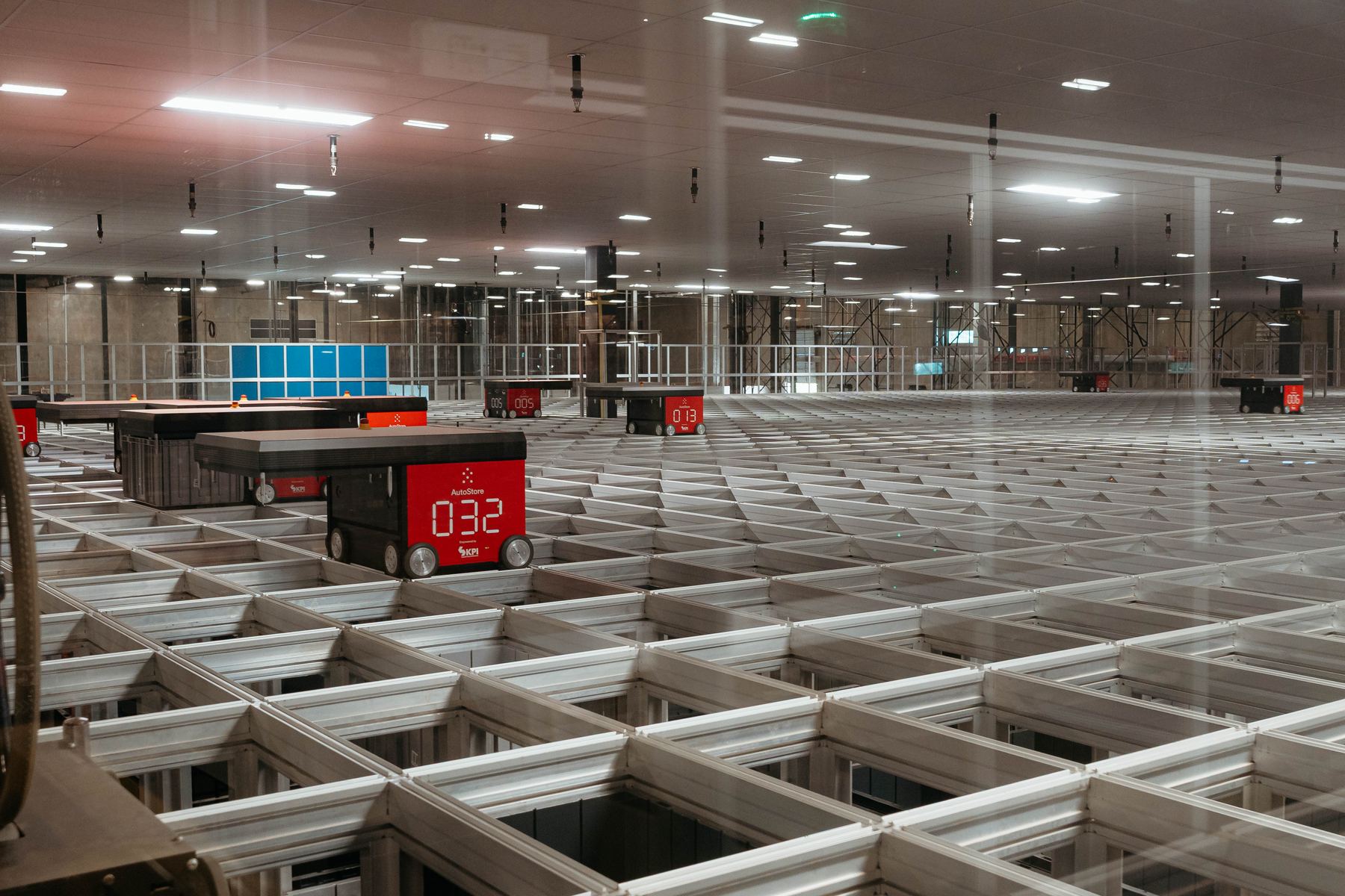Robots working an automated storage grid behind a glass wall in a distribution center